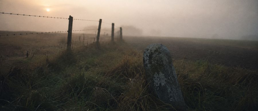 Une borne frontière de pierre à demi enfouie dans un champ, dans la brume