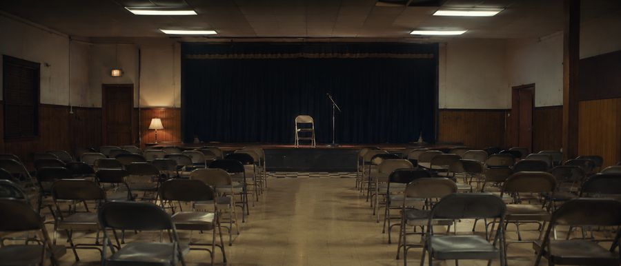 Une salle communale vide avant un meeting, chaises pliantes alignées face à une estrade