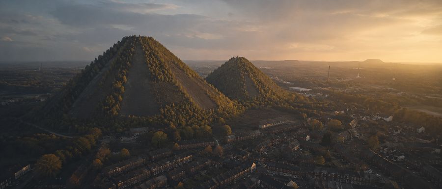 Deux terrils coniques boisés dominant une ville de briques au crépuscule